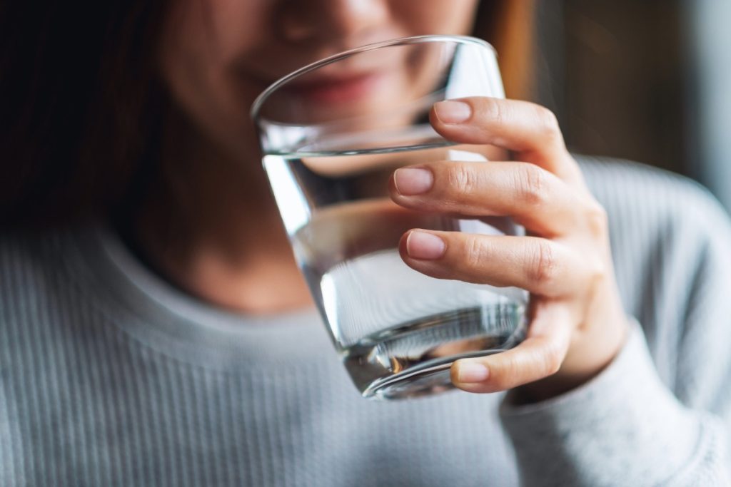 A woman drinking water after eating mushroom gummies